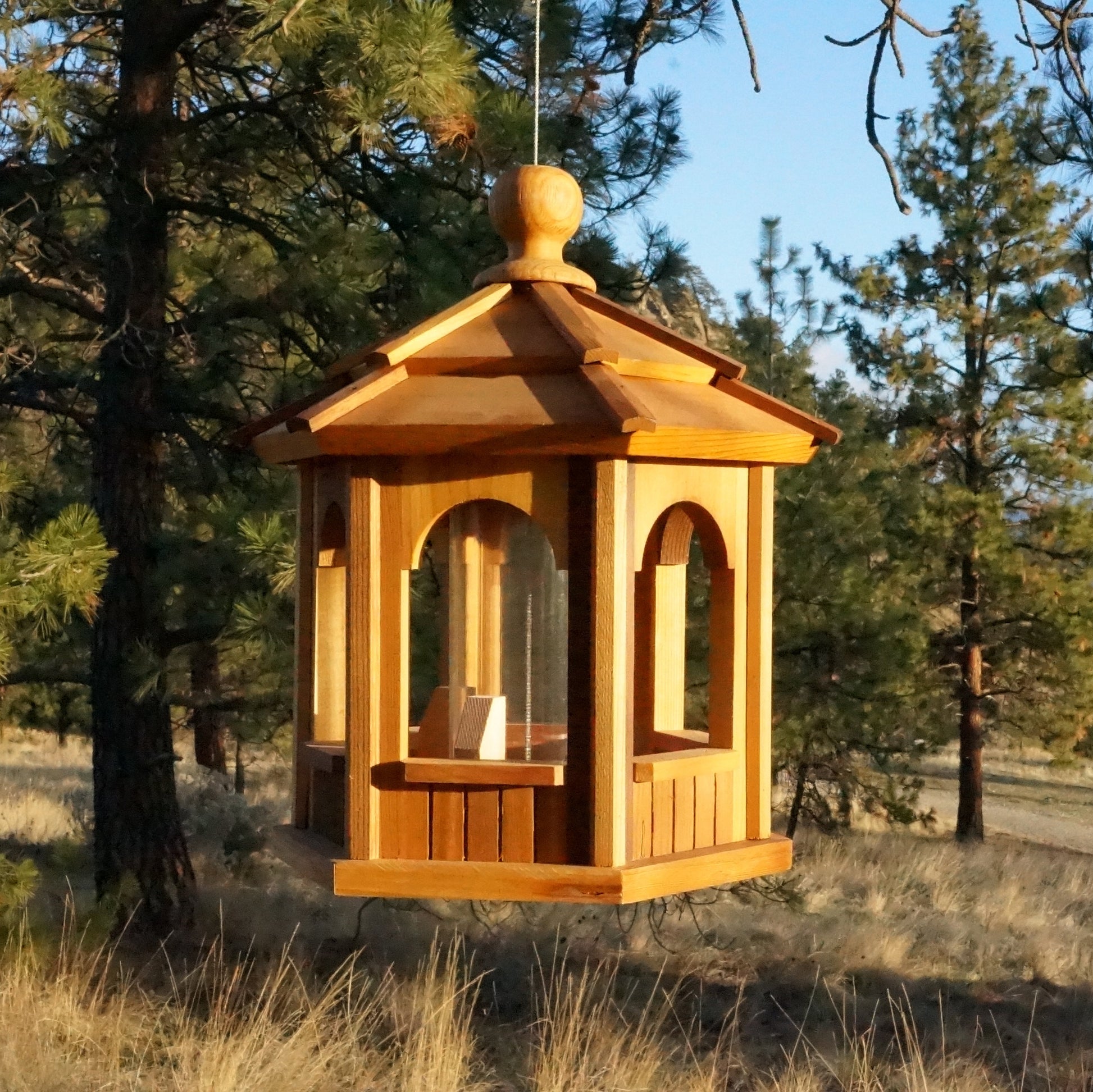 12-inch cedar bird feeder hanging in a lush garden, designed to attract birds while adding elegant outdoor charm, handmade in British Columbia by Kelowna Woodcraft.